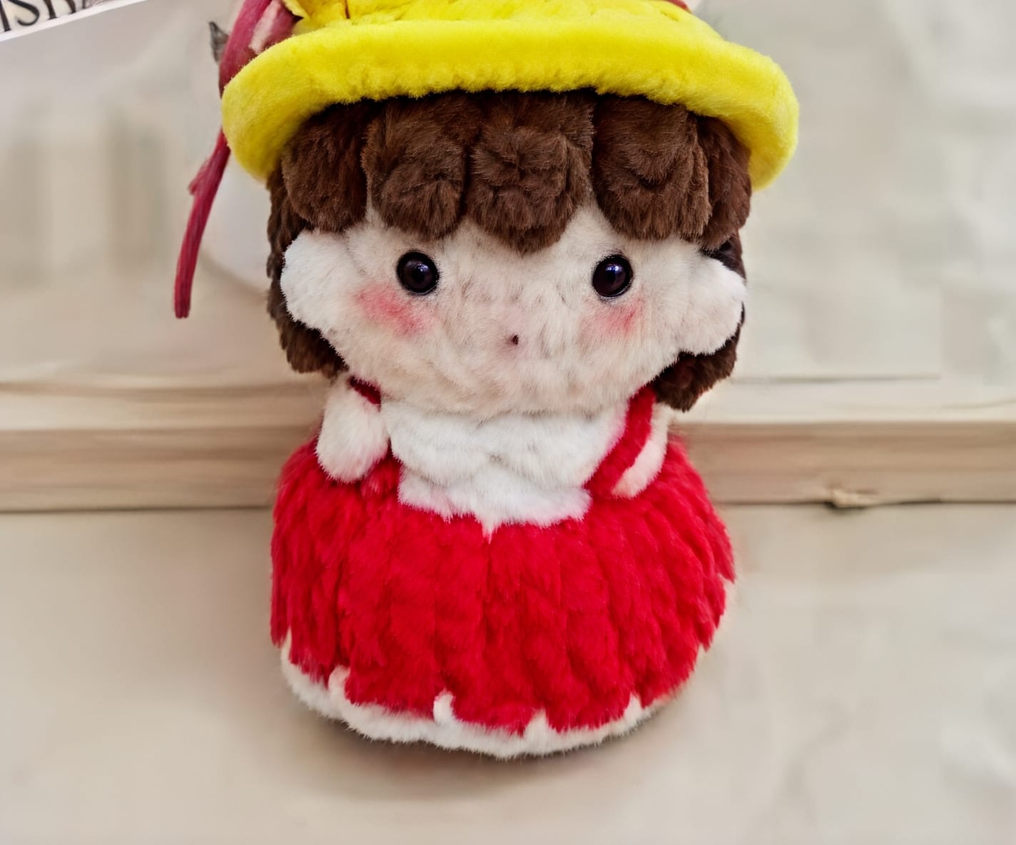 Small plush toy with a yellow hat and red outfit on a light background