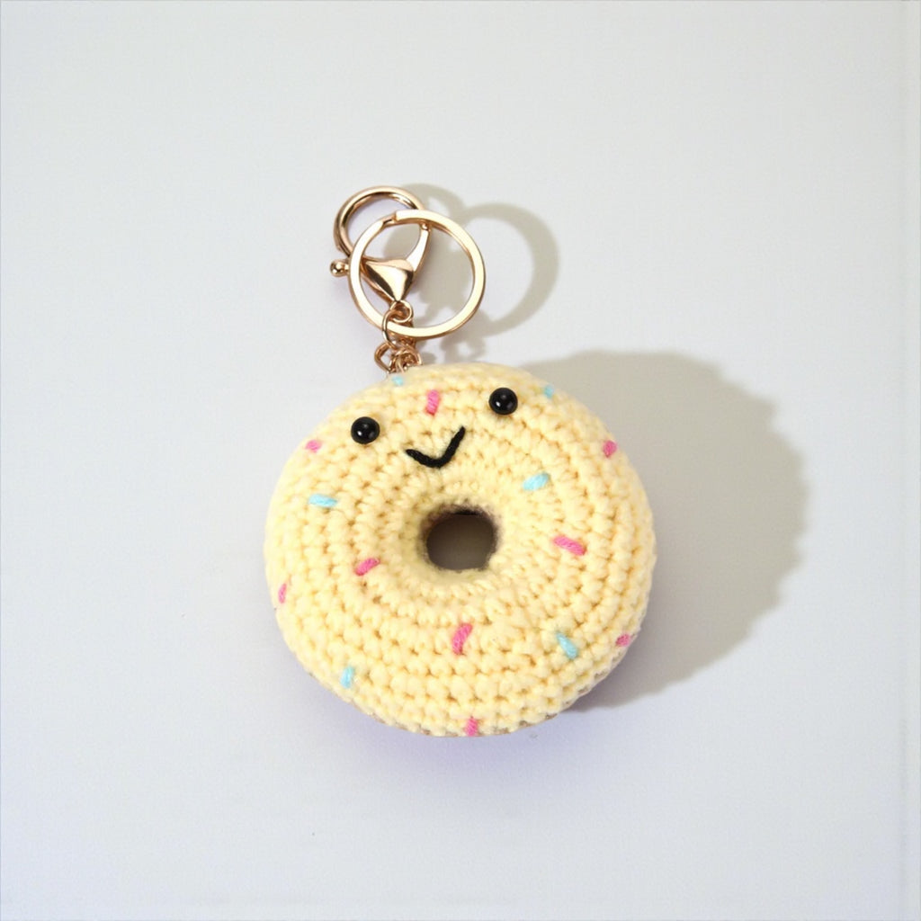 Crocheted donut keychain with a face on a light gray background