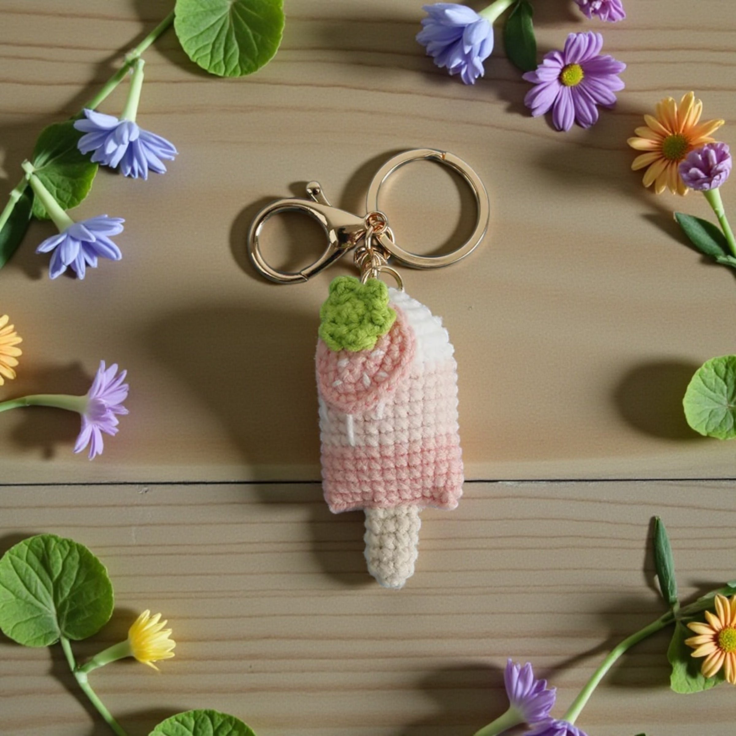 Crocheted keychain with a gradient design on a wooden surface with flowers around.