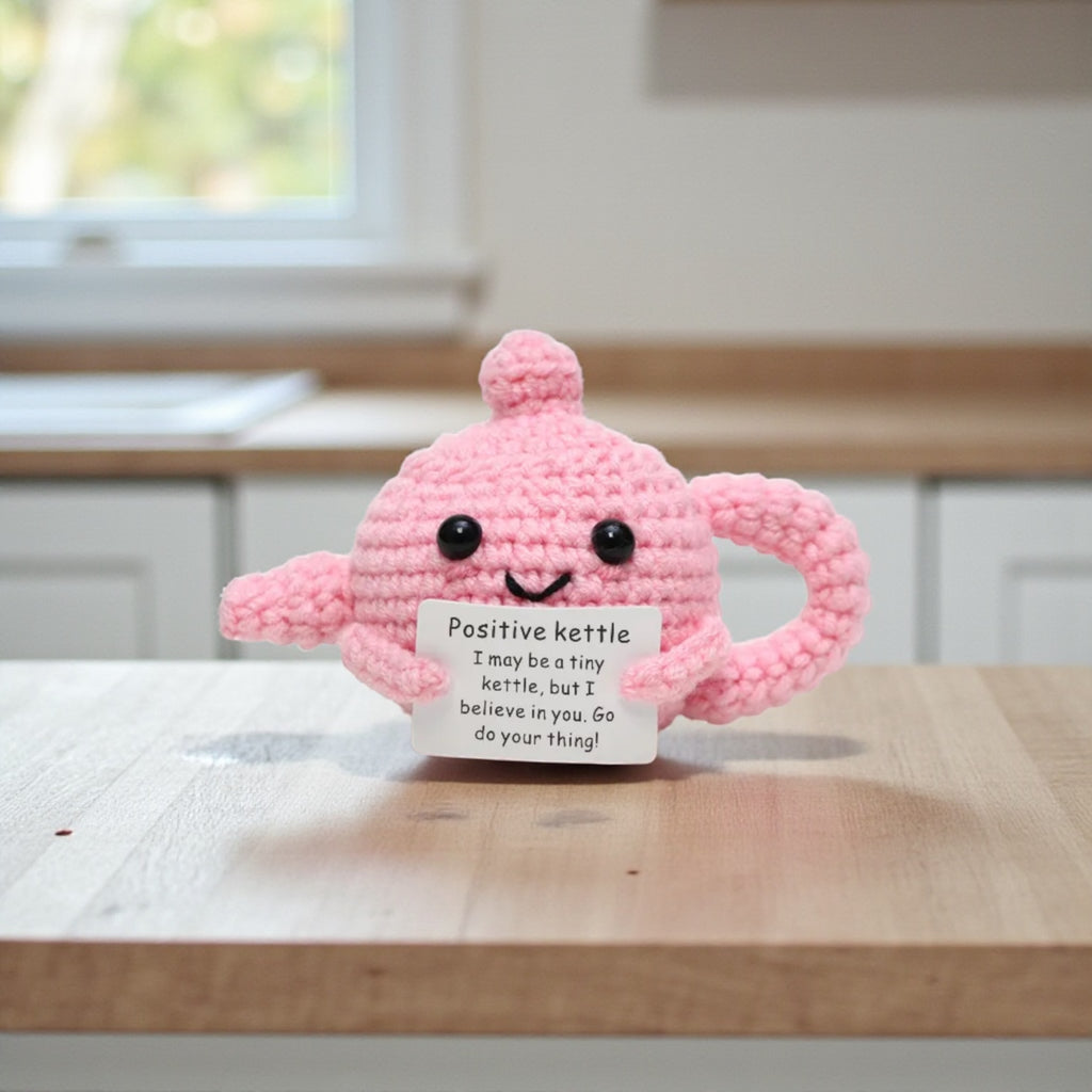 Pink knitted kettle with a small sign on a wooden surface