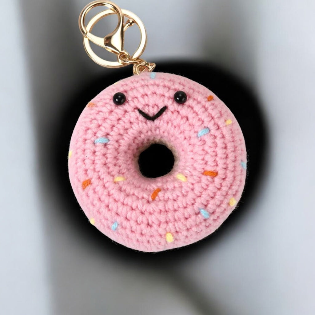 Pink crochet donut keychain with a gold ring on a gray background