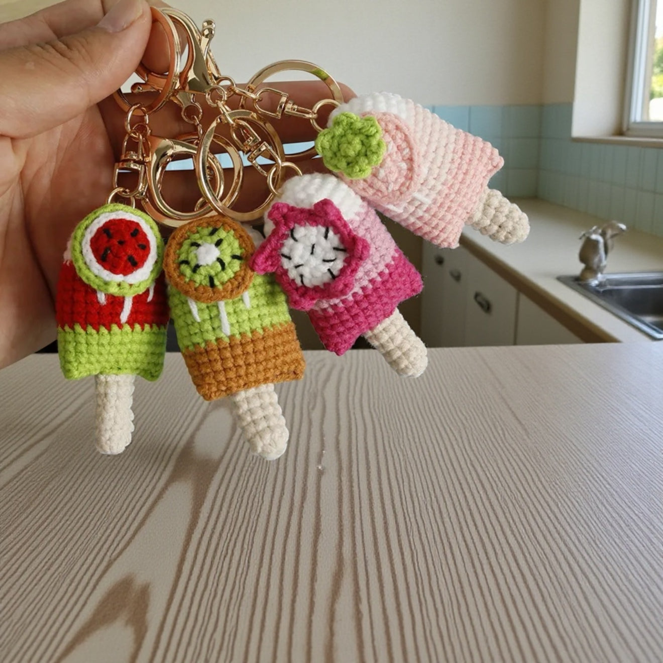 Handmade crochet keychains shaped like ice cream cones held over a kitchen counter.