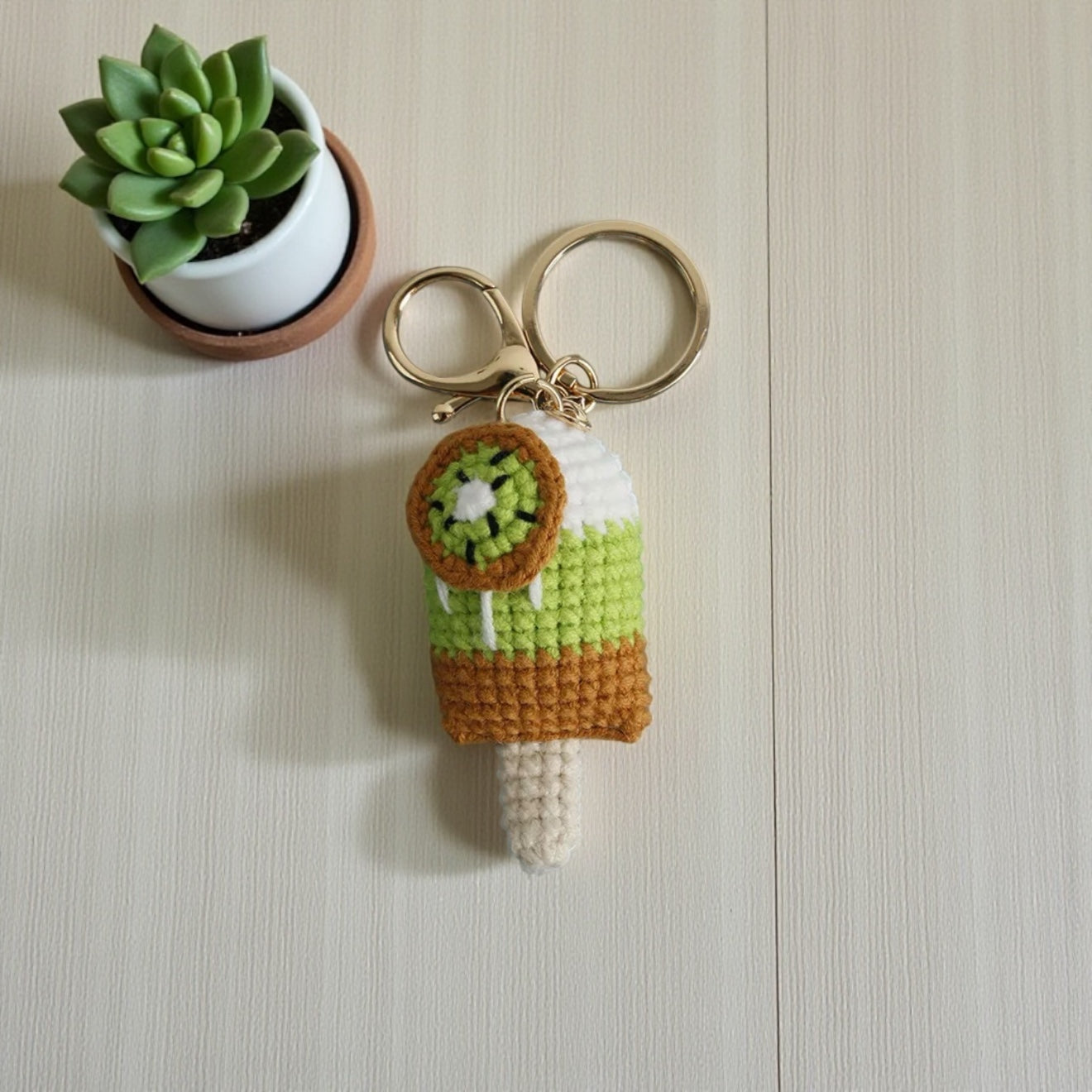 Crocheted ice cream keychain with a small plant on a neutral background