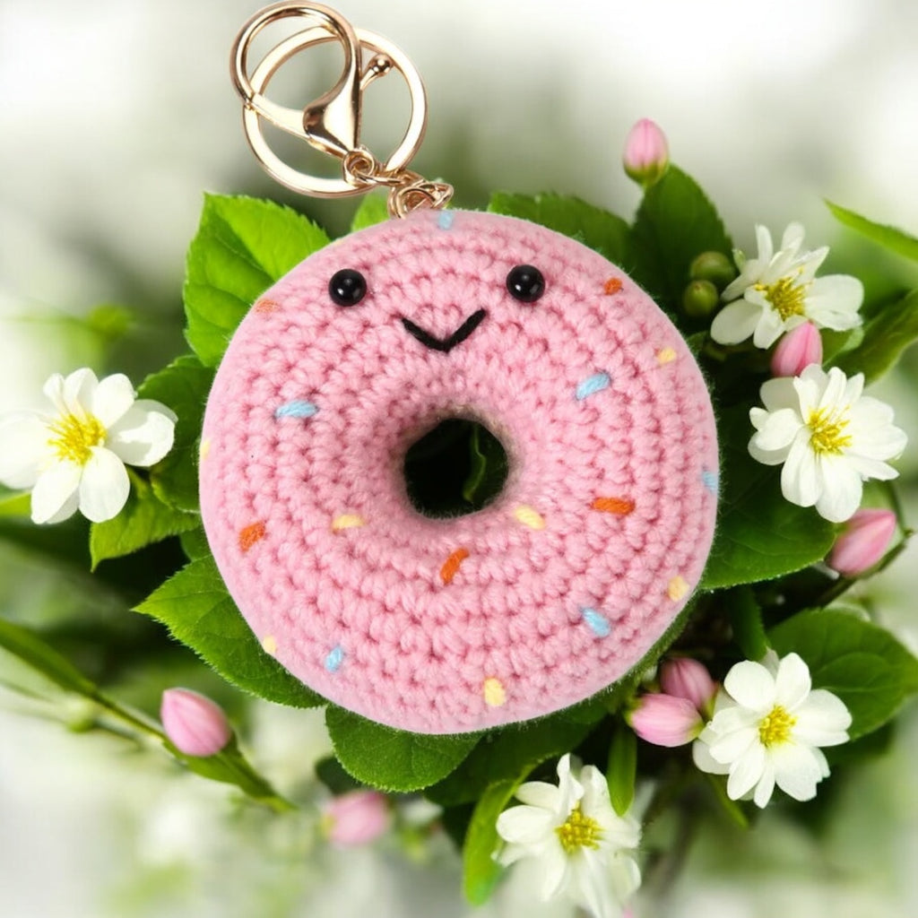 Pink crocheted donut keychain with sprinkles on a floral background