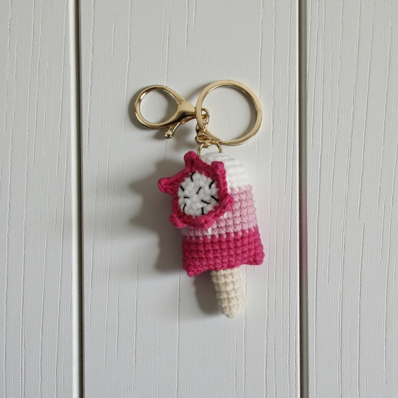 Crocheted ice cream cone keychain with pink cover on a light wooden background