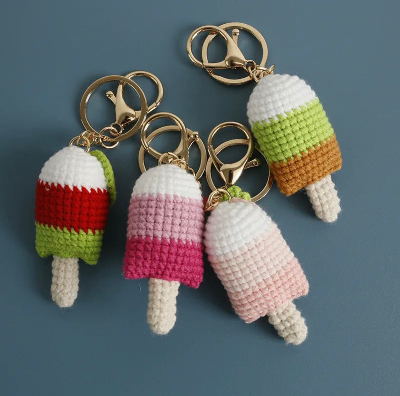 Crocheted ice cream keychains on gold rings against a blue background