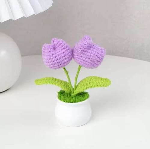 Crocheted purple tulips in a white pot on a light surface with a neutral background