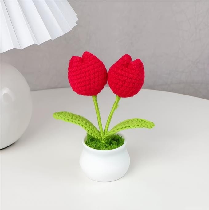 Crocheted red tulips in a white pot on a light surface with a neutral background