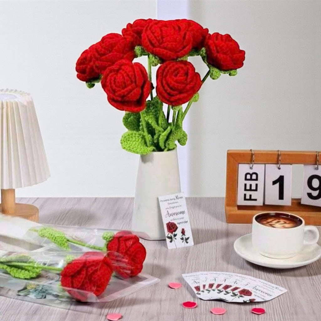 Bouquet of red knitted flowers in a vase on a table with a cup of coffee and calendar.