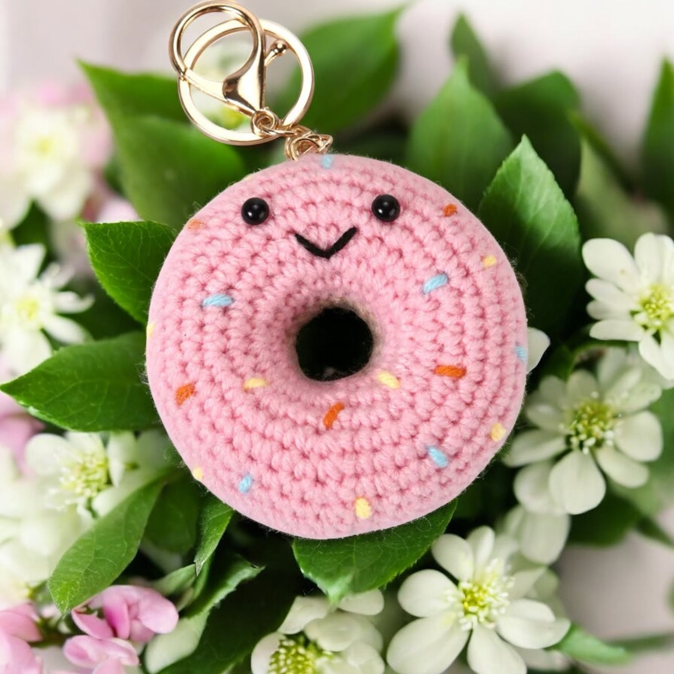 Pink crochet donut keychain with sprinkles on a floral background