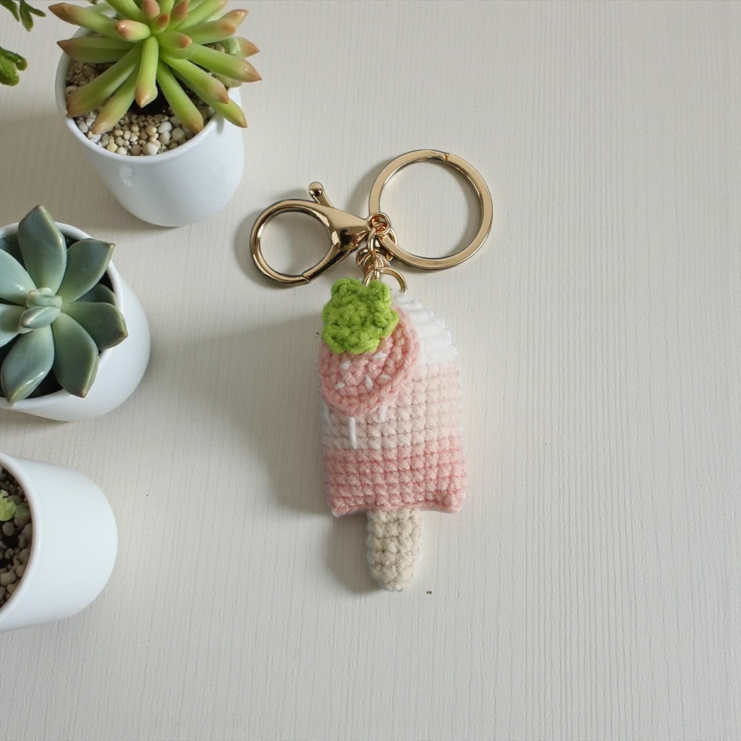 Crocheted keychain shaped like a popsicle with a small green plant on a light surface.