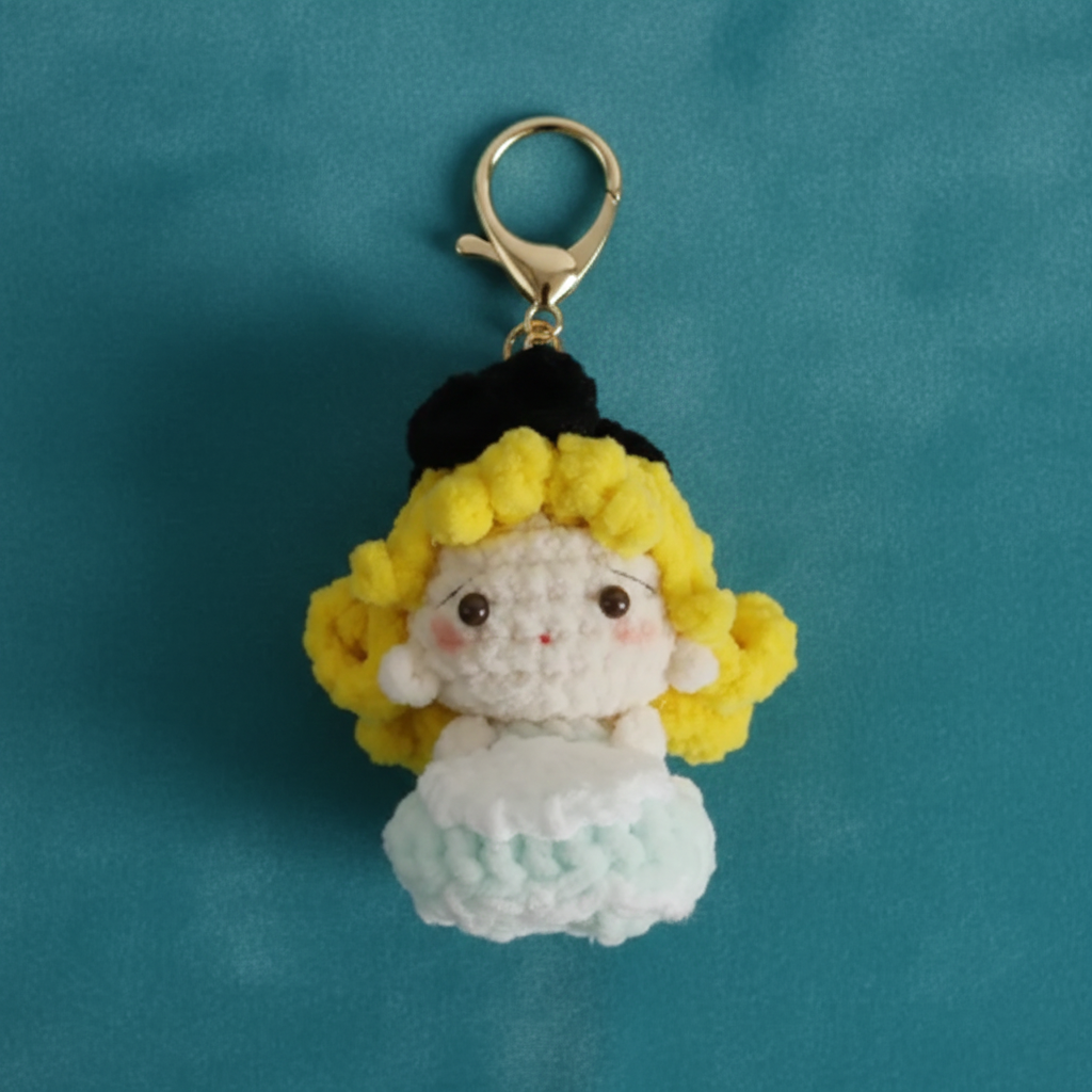 Crocheted character keychain with yellow hair and white dress on a teal background