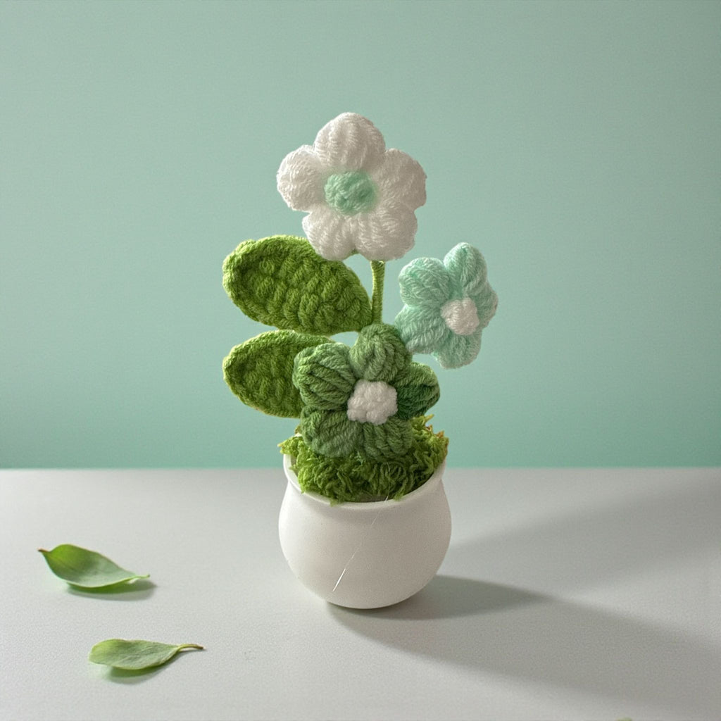 Crocheted flower arrangement in a white pot on a light gray surface with a light green background