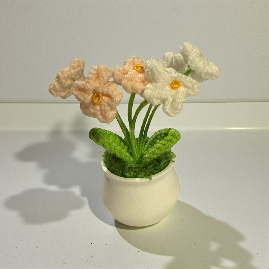 Knitted flowers in a pot on a white surface