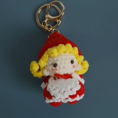 Crocheted keychain of a character with red outfit, yellow hair, and white face on a dark blue background.