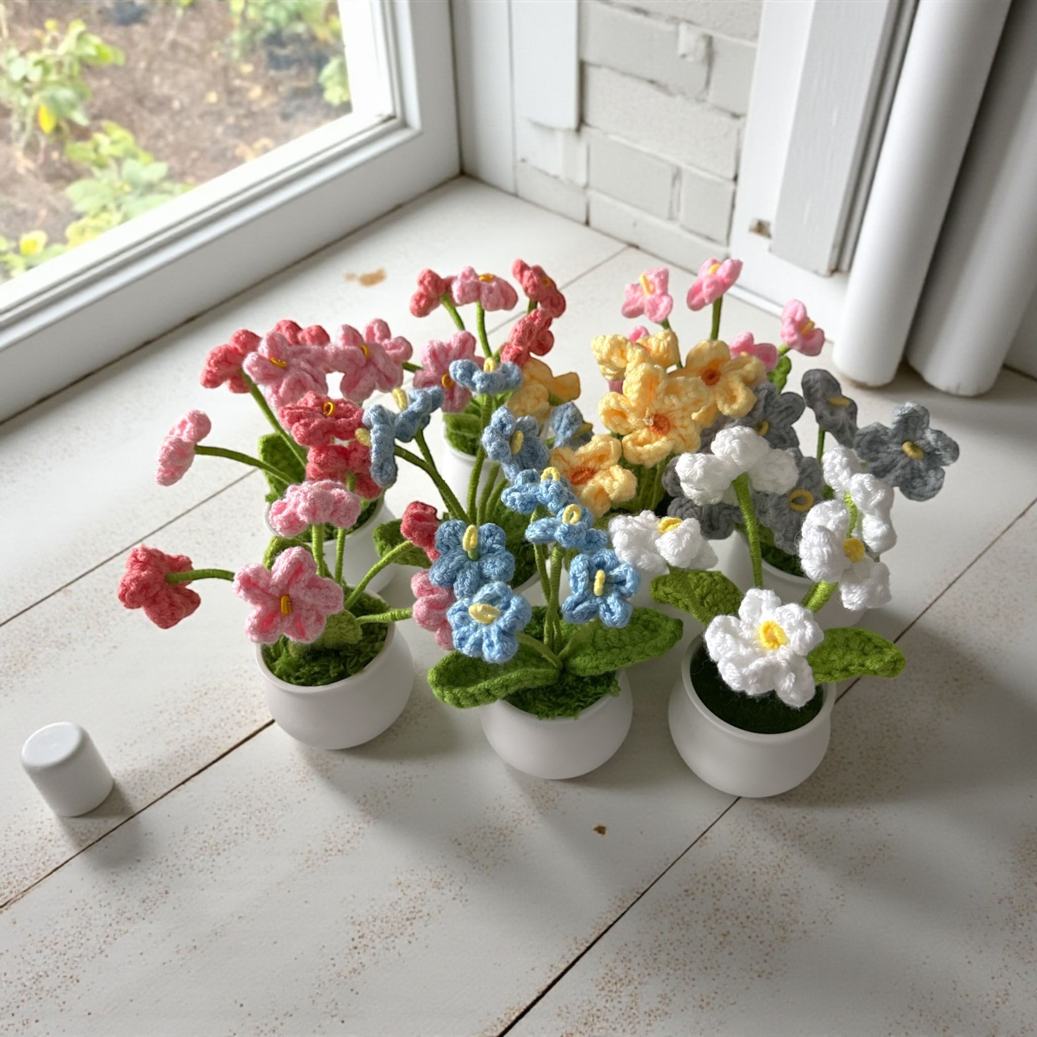 Colorful artificial flowers in white pots on a tiled floor near a window.