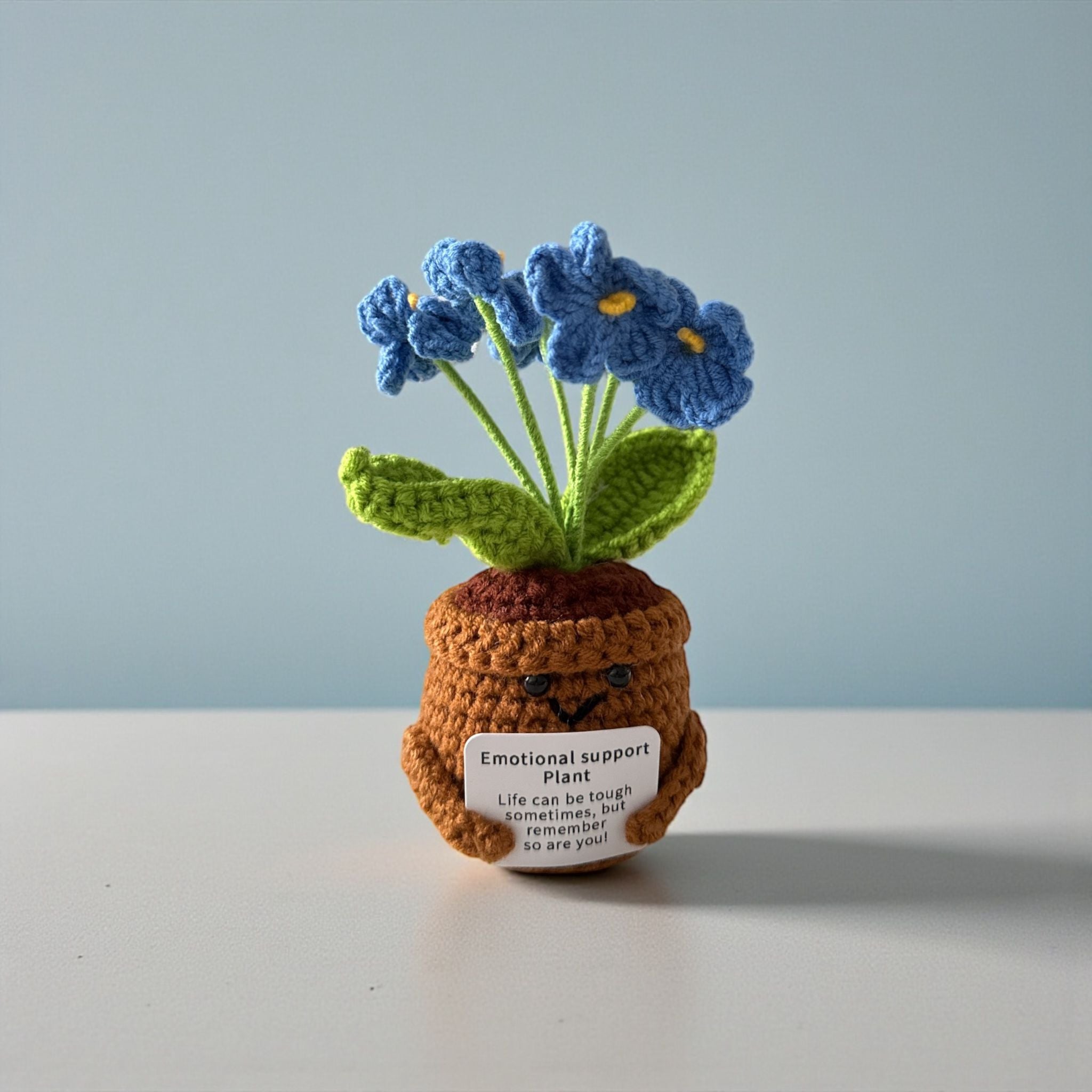 Crocheted potted plant with blue flowers on a plain background