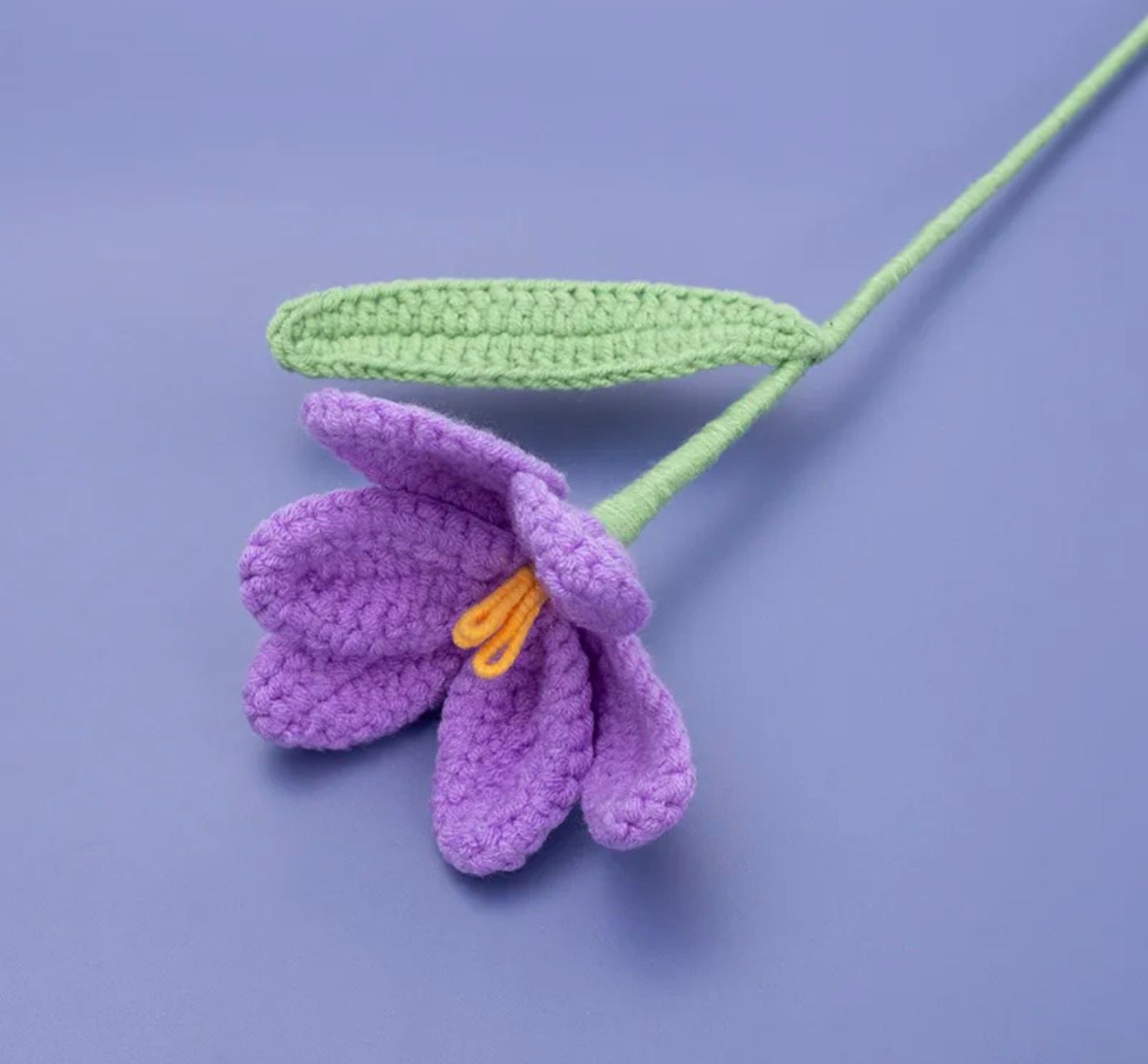 Crocheted purple flower with a green stem on a purple background