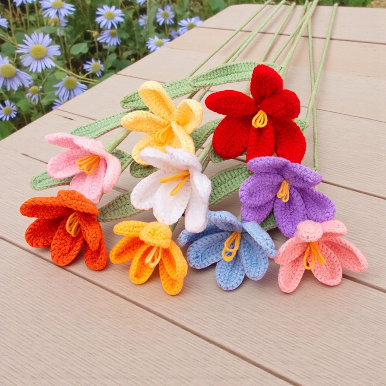 Colorful crocheted flowers on a wooden surface with a garden background
