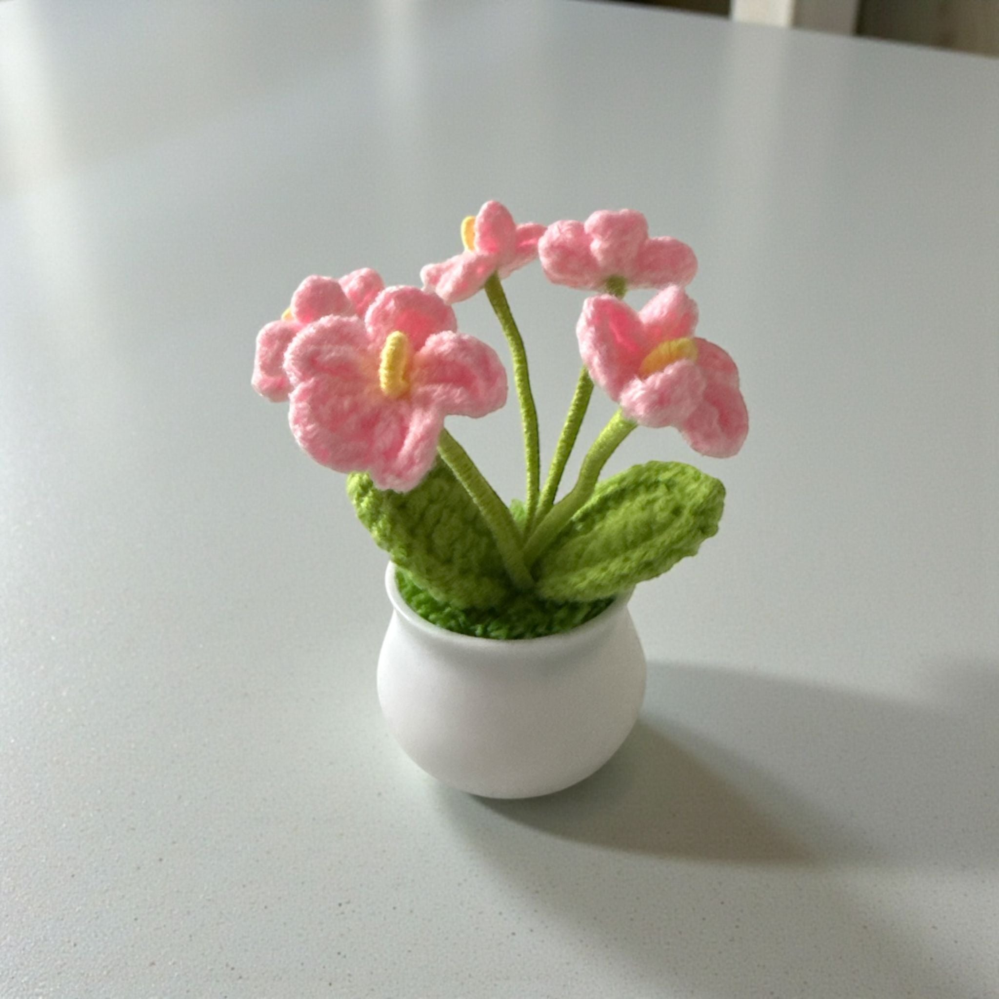 Knitted pink flowers in a white pot on a light gray surface