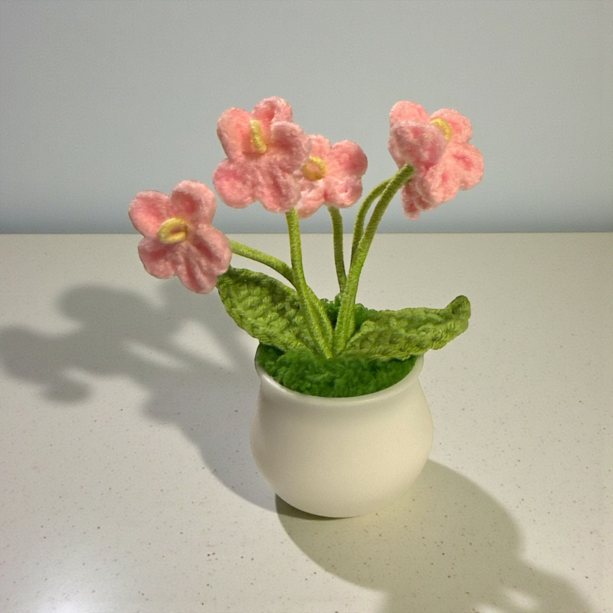 Knitted pink flowers in a white pot on a light surface with a gray background