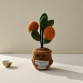Crocheted potted plant with orange fruits and green leaves on a neutral background