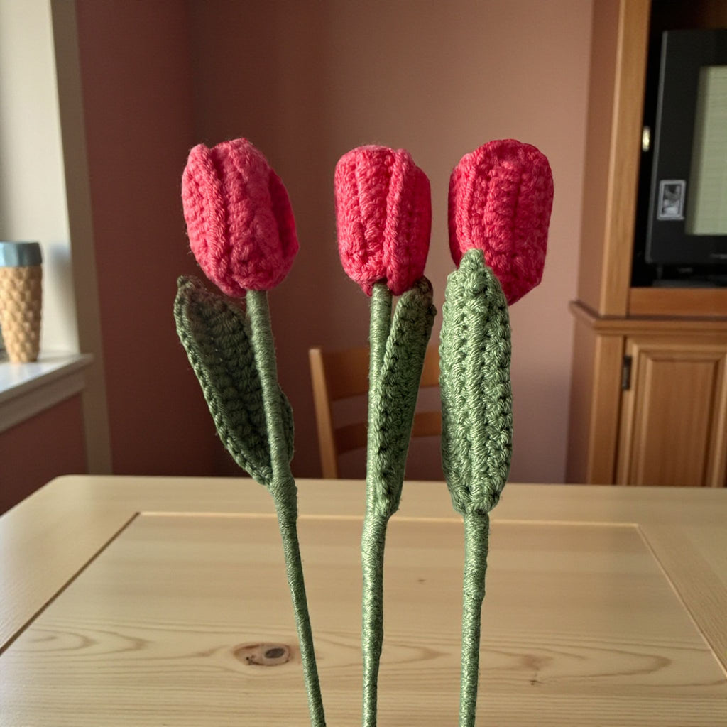 Three knitted tulips on a wooden table with a blurred indoor background