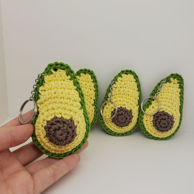 Three crocheted avocado keychains held by a hand on a white background