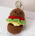 Crocheted hamburger keychain with a smiling face on a white surface.