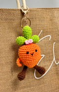Crocheted carrot keychain with a face on a brown fabric background