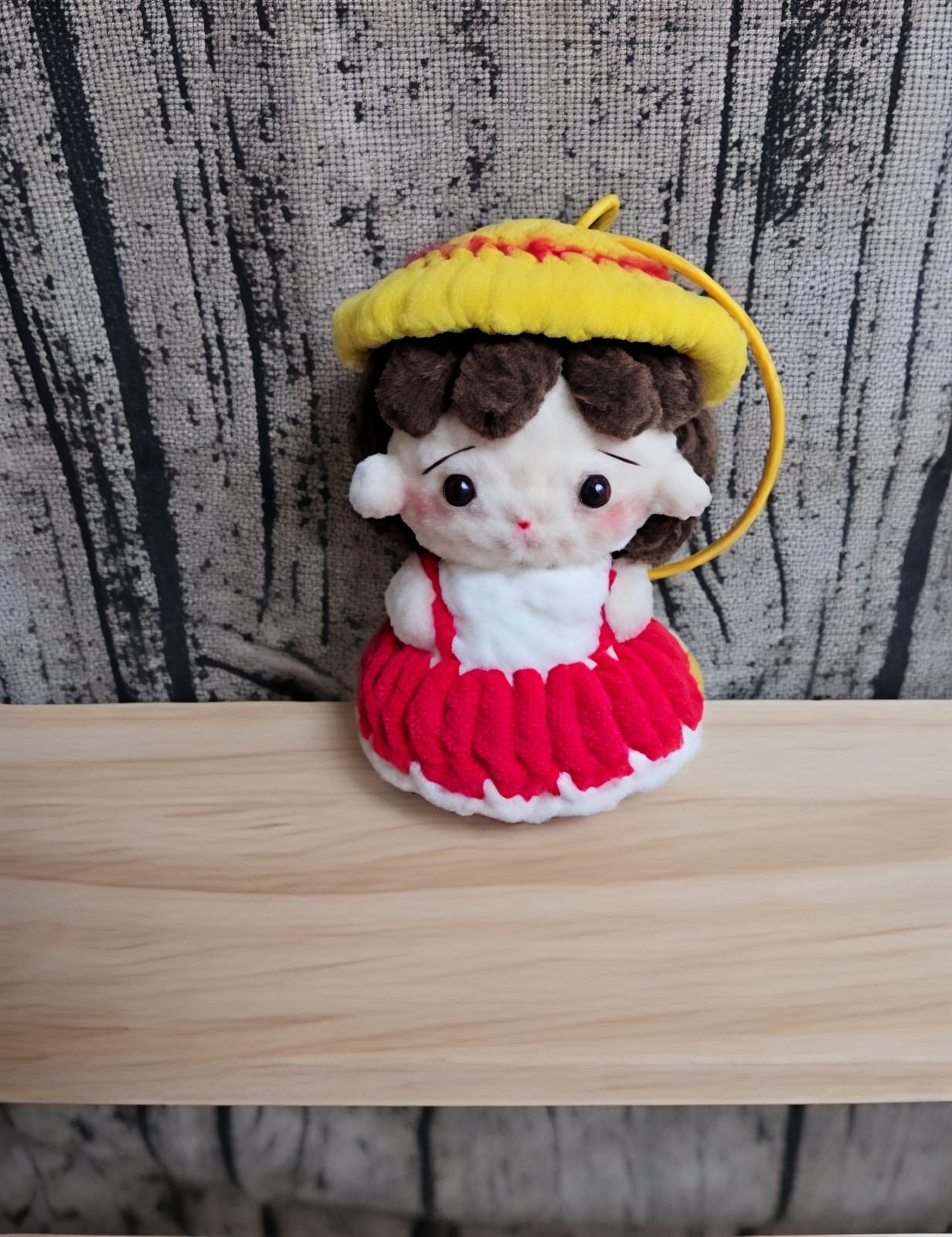 Small plush toy with a yellow hat and red dress on a wooden surface with a textured background