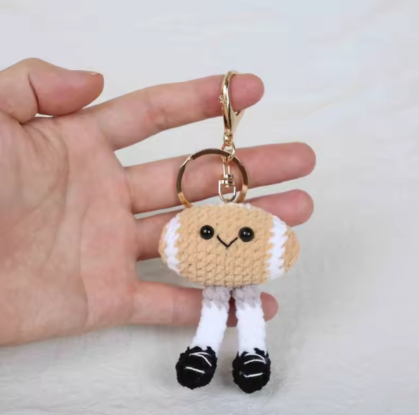 Hand holding a small crochet keychain with a face on a plain background