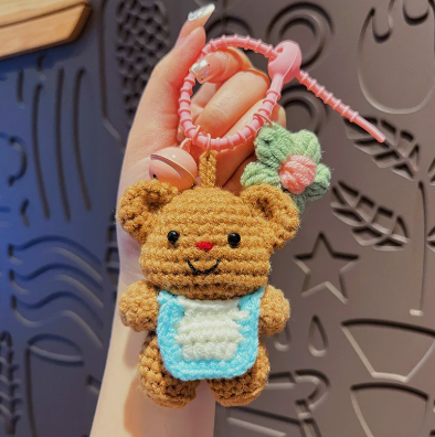 Hand holding a small crochet teddy bear keychain with a textured background
