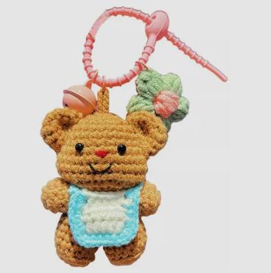 Crocheted teddy bear keychain with a pink ribbon on a white background