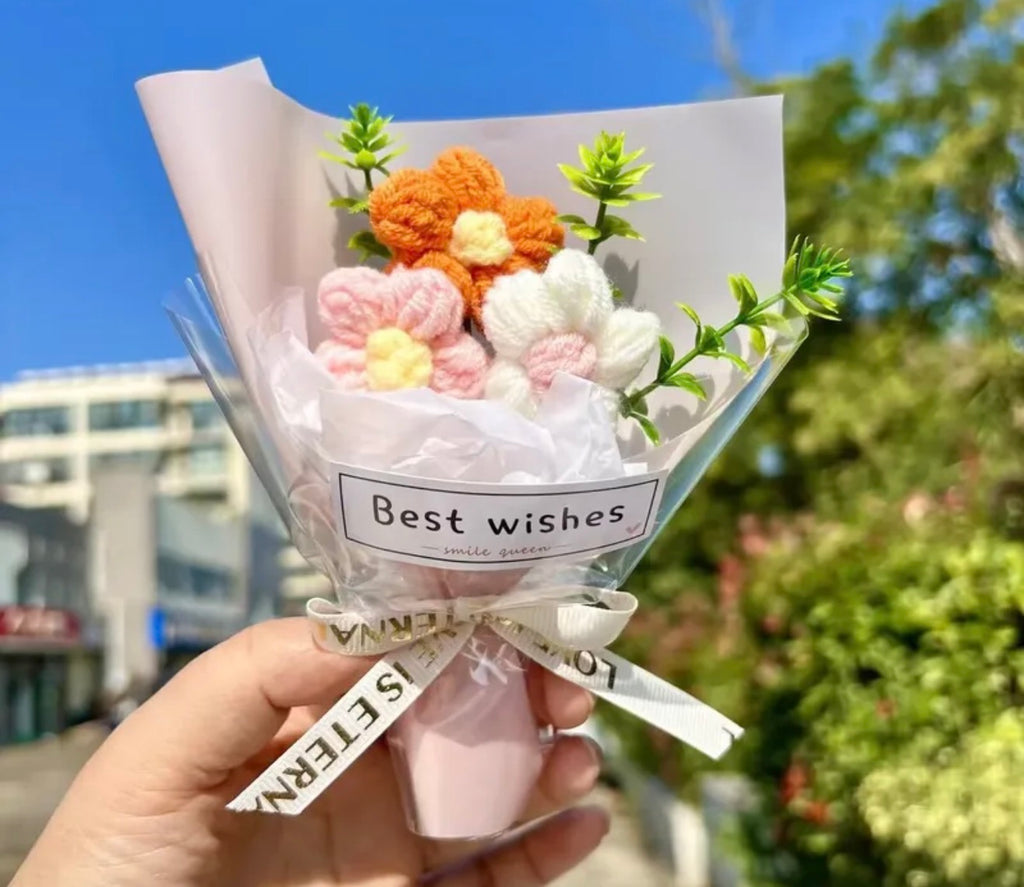 Bouquet of knitted flowers with a 'Best wishes' card held outdoors.