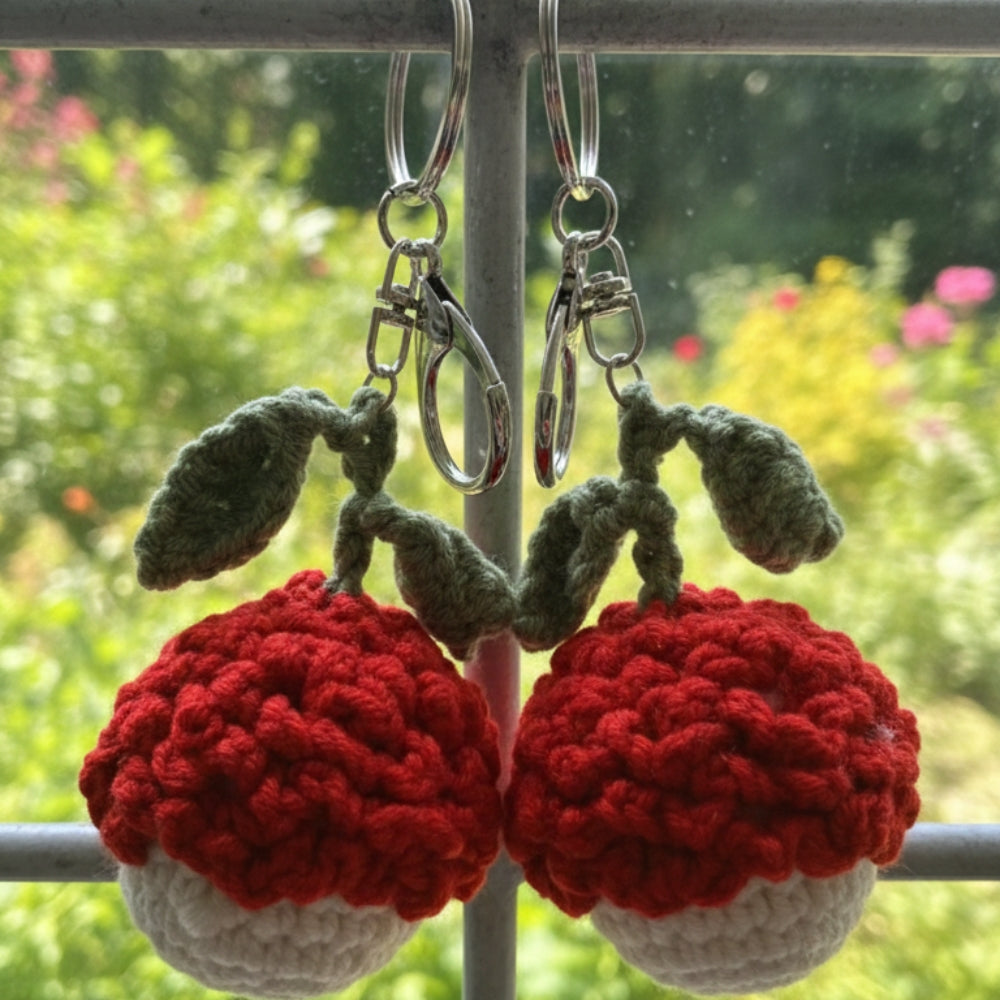 Crocheted cherry keychains hanging outdoors with a garden background