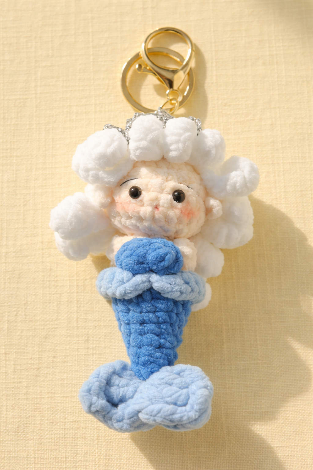 Crocheted keychain with a character holding a blue object on a beige background