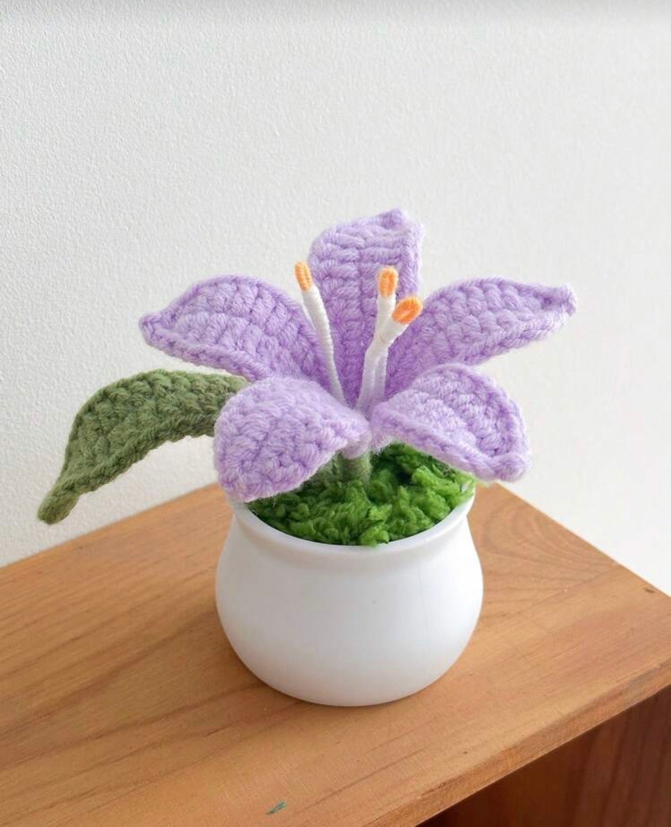 Crocheted purple flower in a white pot on a wooden surface with a light background