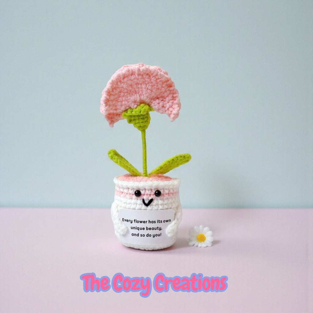 Crocheted flower pot with a pink flower on a light gray background, featuring 'The Cozy Creations' branding.