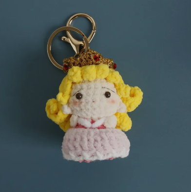 Crocheted keychain of a princess with yellow hair and a crown on a blue background