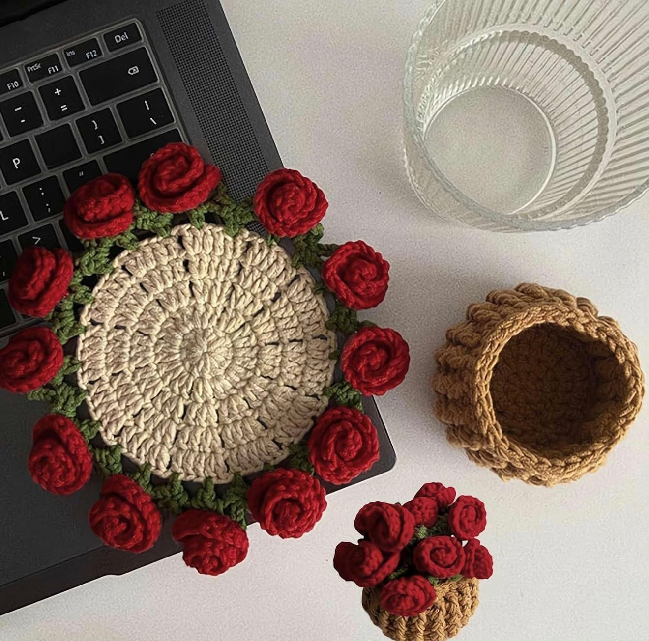 Crocheted items including a coaster with red roses and a small basket on a white surface.
