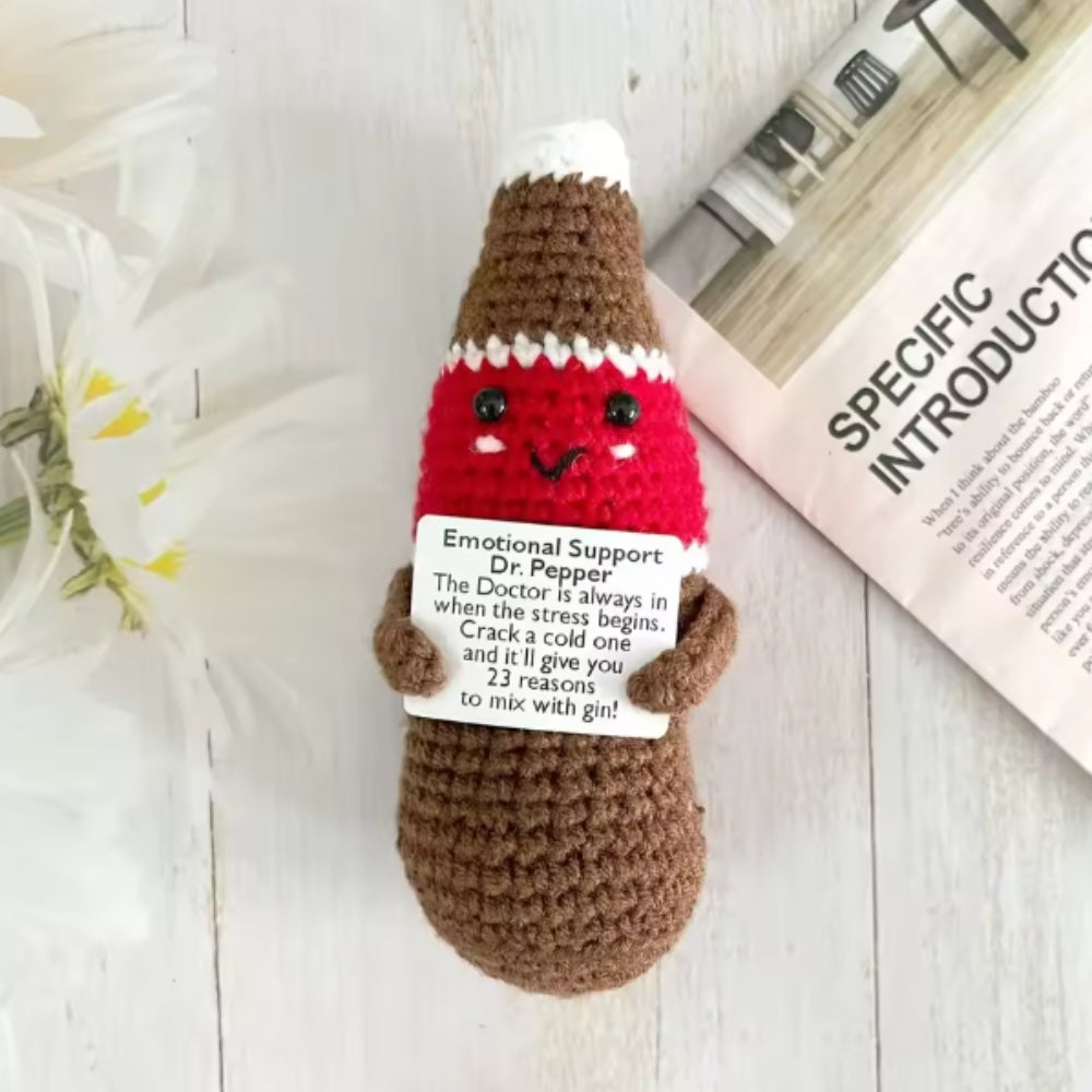 Crocheted Dr Pepper bottle plush toy with a label on a light wooden surface.