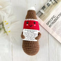 Crocheted Dr Pepper bottle plush toy with a label on a light wooden surface.