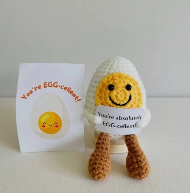 Crocheted egg-shaped character with a card that reads 'You're EGG-cellent!' on a white background.
