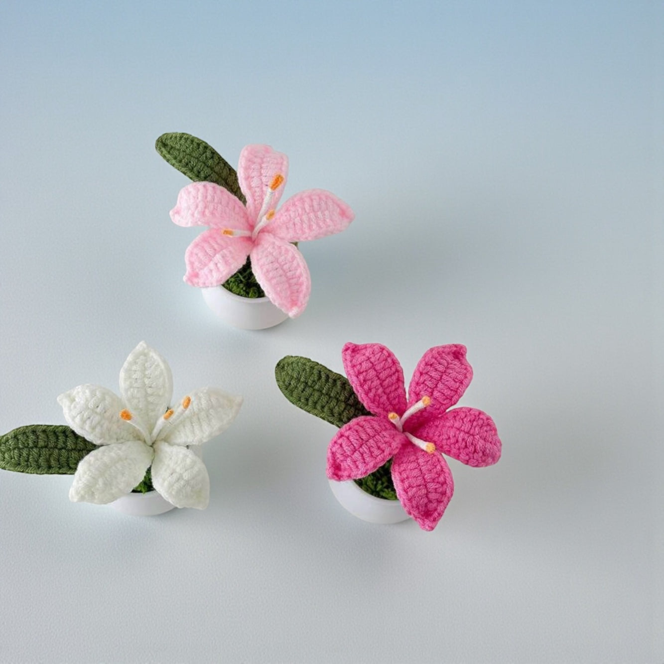 Three crocheted flowers in pink, white, and green on a light gray background