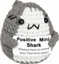 Crocheted shark plushie with a sign saying 'Positive Mini Shark' on a white background