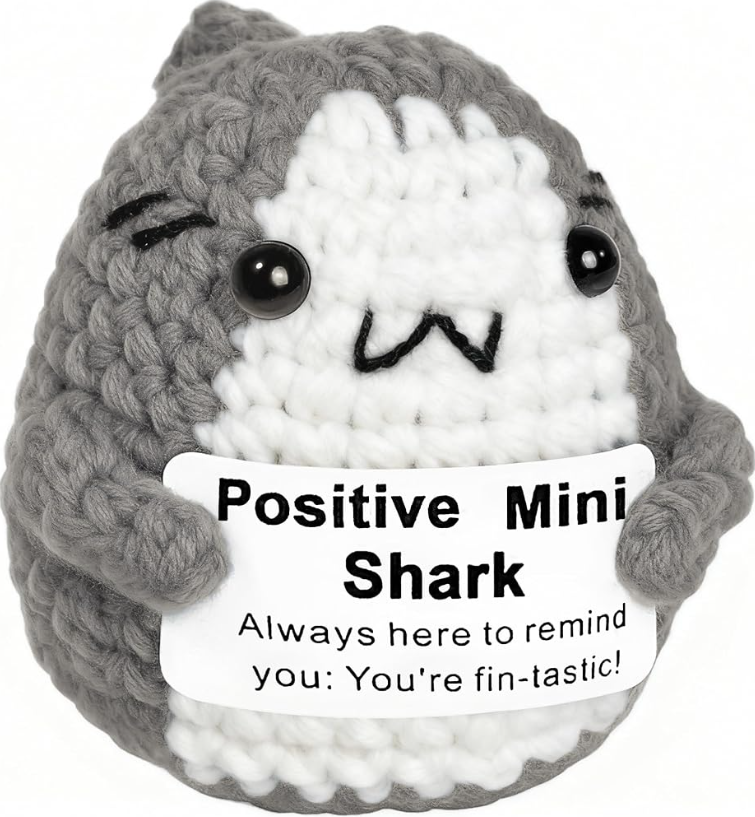 Crocheted shark plushie with a sign saying 'Positive Mini Shark' on a white background