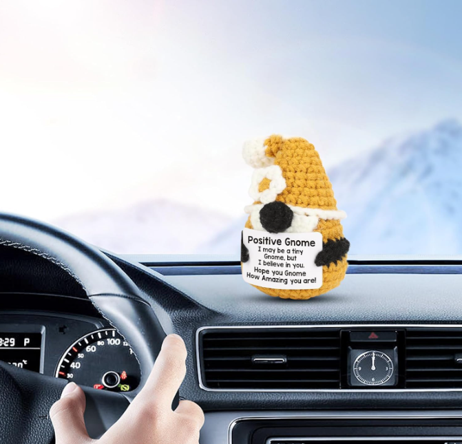 Crocheted gnome plush toy on a car dashboard with a scenic background