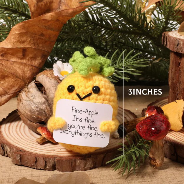 Small yellow plush toy with a message card on a wooden surface with Christmas decorations.