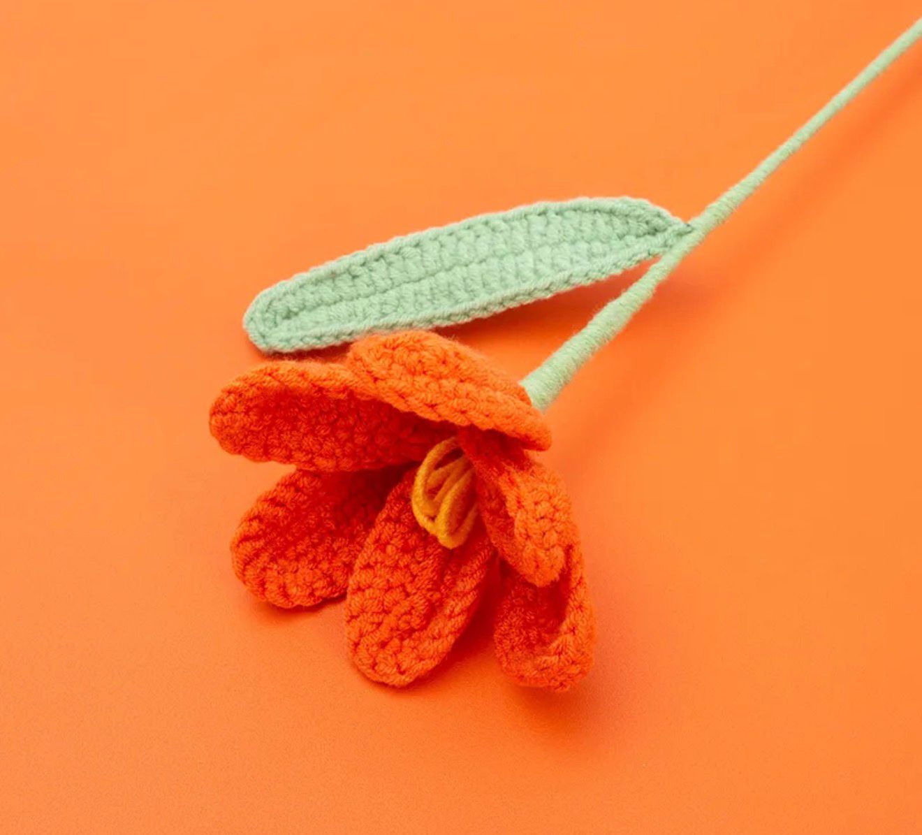 Crocheted orange flower with green stem on an orange background